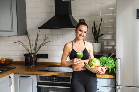 Vegetable smoothie detox in the hands of a young woman, she is in sportswear in the kitchenの写真素材