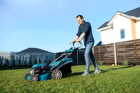 A handsome guy is mowing a lawn with a gasoline lawn mower and smilesの写真素材