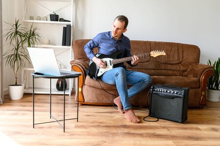Online studying, webinars. A young man is shows how to play electric guitar to laptop webcamの写真素材