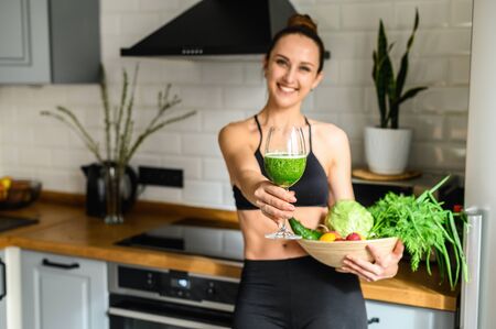 Vegetable smoothie detox in the hands of a young woman, she is in sportswear in the kitchenの写真素材