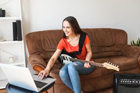 Online learning concept. Young woman watching video tutorials and learning to play the electric guitar, uses a combo amplifierの写真素材