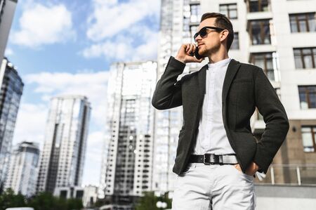 Successful young businessman in a smart casual speaks on the phone among the skyscrapers, sunglasses on itの写真素材