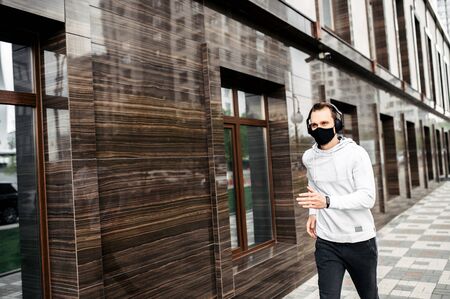 Healthy habits during quarantine. Young man in sports clothing in medical mask on the face is running while exercising outsideの写真素材