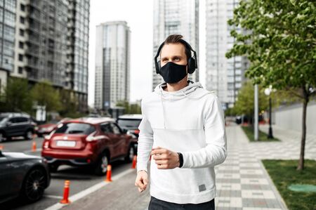 Keep in shape during quarantine. A young man in sports clothing is running in the city outsideの写真素材