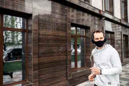 Healthy habits during quarantine. Young man in sports clothing in medical mask on the face is running while exercising outsideの写真素材