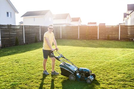 A handsome guy is mowing a lawn with a gasoline lawn mower and smiles, he is in sunglassesの写真素材