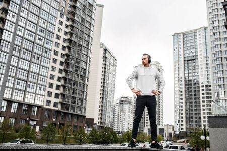 Be stronger. Young athletic guy in sportswear is resting after workout outdoors in a town landscapeの写真素材