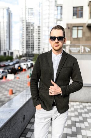 Vertical portrait of young stylish guy outdoors. The guy in sunglasses in smart casual clothes looks at cameraの写真素材