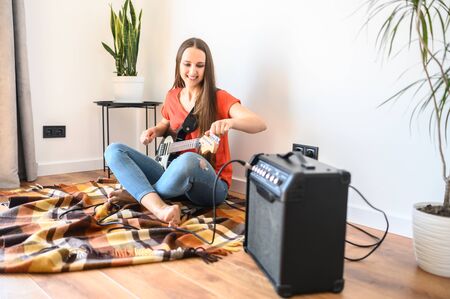 A young woman is playing an electric guitar at home using a combo amplifier. Leisure at home during quarantine, stay homeの写真素材
