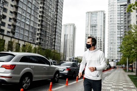 Keep yourself in shape during quarantine. Athletic young man is jogging in a protective mask among high-rise buildings. Healthy lifestyle conceptの写真素材