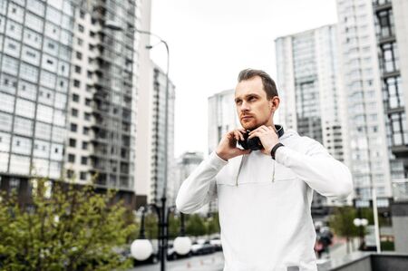 Sports lifestyle. Young athletic man in sportswear with headphones among city skyscrapersの写真素材