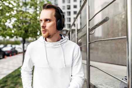 Workout outdoors. Young athletic guy in sportswear with headphones runs in an urban landscapeの写真素材