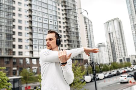 Young man does stretching while exercising outdoors. Urban landscape on backgroundの写真素材