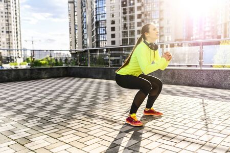 A young woman in sportswear is warming up before outdoors workout among skyscrapers. She doing...