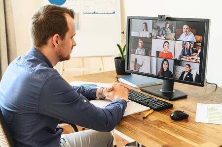 Virtual conference with employees. A young man in formal shirt using pc for video call, he has video meeting with several people together. Remote work conceptの写真素材