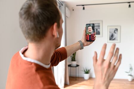 A male friends are talking online via video while staying at home. A guys is using smartphone for...