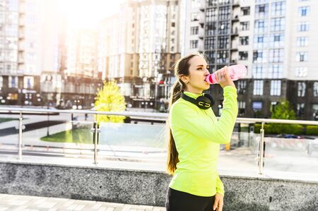 Quenching thirst on a street workout. Fitness woman is drinking water from sports water bottle outdoors.の写真素材