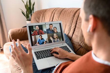 Virtual meeting with a friends. A guy is using laptop for video call, he lays on couch and talks at easeの写真素材