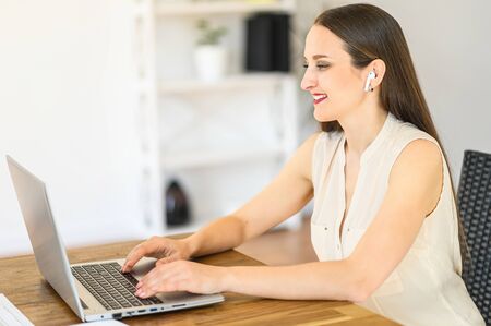 Close up a young attractive woman with airpods is using laptop for work in home office. Side viewの写真素材