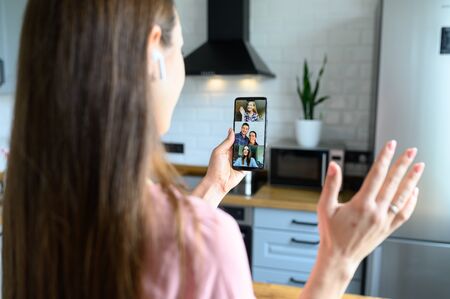 Young positive woman communicates via video communication using a phone, she waving hello to the friends at the screen. Self-isolation during quarantine. Video communication, zoom.の写真素材