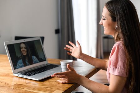 Distance communication with friends via video call, zoom. A young attractive woman talking via video with her friend, she looks at webcamerra with smile. Side viewの写真素材