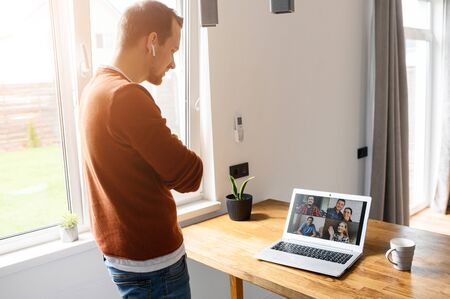Virtual meeting, online conference with coworkers. A young man is using laptop app for video communication with several people togetherの写真素材