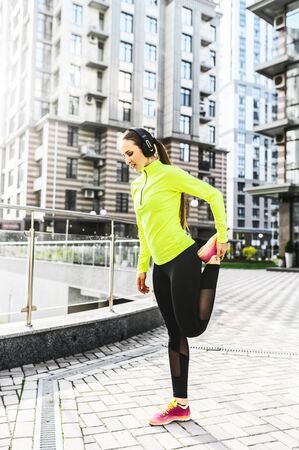 Full length young woman in sportswear is doing stretching exercises outdoors, she is warming up before workout. Healthy lifestyle conceptの写真素材