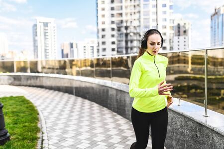 A girl in sportswear with headphones on her head is running in the city street. Healthy lifestyle...
