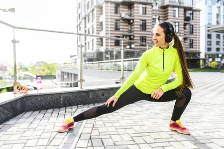 Full length young woman in sportswear is doing stretching exercises outdoors, she is warming up before workout. Healthy lifestyle conceptの写真素材