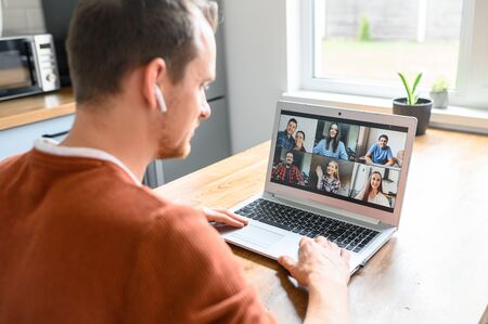 A guy is using app for video conference, video call on laptop. He talks online with a several friends together. Side viewの写真素材