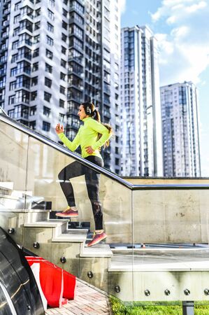 Street workout. A young woman in sportswear is running up stairs. Urban landscape on backgroundの写真素材
