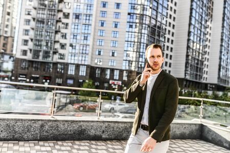 A young attractive man in smart casual wear with is talking on the phone in the downtown. Solutions of business tasks on phoneの写真素材