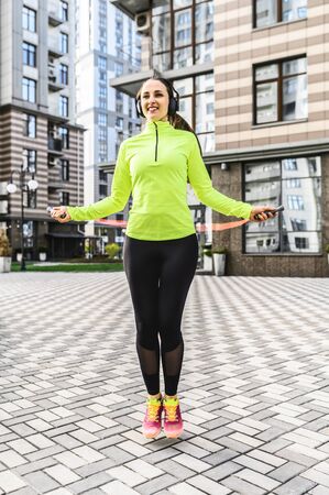 Outdoor cardio workout. A young girl in sportswear is jumping with a skipping rope on the streetの写真素材