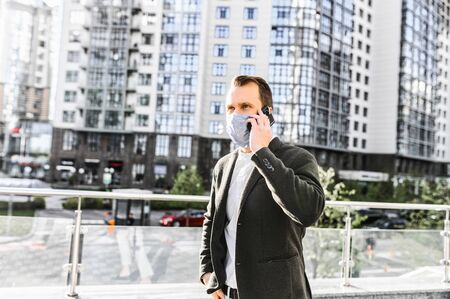 A guy in smart casual wear with a surgery protective mask on the face is talking on the phone in the downtown. Stay safety during quarantine, epidemiaの写真素材