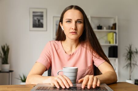 Webcam view of concentrated young attractive girl in casual wear at home, she typing on the keyboard with a serious face and watching intently on the screen. Front viewの写真素材