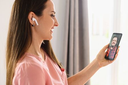 Zoom, video call, video chat. An attractive young woman is using smartphone for online video communication with a friend. Side viewの写真素材