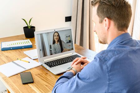 Video call. A guy in smart casual shirt using laptop for talking with a woman via video. Rear viewの写真素材