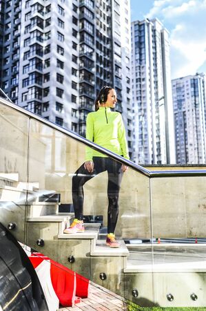 Street workout. A young woman in sportswear stands on a concrete stairs. Urban landscape on backgroundの写真素材