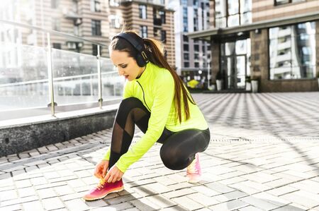 A woman in sportswear is going to run outdoors. She is tying shoelaces on a trendy runners sneakers. Healthy lifestyle conceptの写真素材