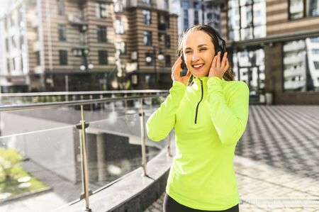 Favorite soundtracks for workout, for running. Young sports girl in sportswear listens to music on headphones and smilesの写真素材