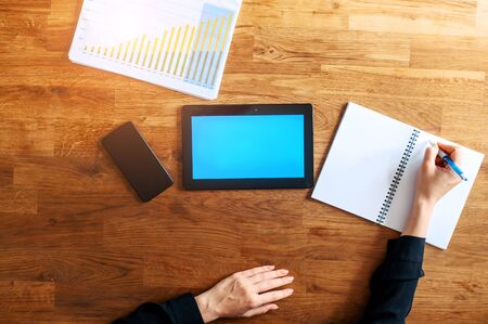 Flat lay female hand is writing syllabus in a notebook and touches digital tablet. A screen of tablet is blank, copy space for text. Online learning concept, webinarsの写真素材