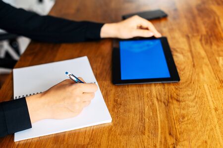 Online study concept, online classes. Close-up a hand of woman is writing abstract in notebook, a digital tablet with blank screen on the backgroundの写真素材