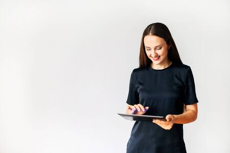 An attractive woman in black color t-shirt is using a tablet, she is touching screen and smiles, isolated on a white background. Concept of technology, digitalizationの写真素材