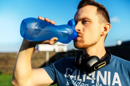 The guy quenches thirst during an outdoor workout. He drinks water from a sports bottleの写真素材