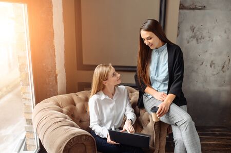Friendly atmosphere in the team. The girl explains something to her colleague, showing the laptop screen. They are in a bright creative office.の写真素材