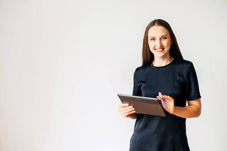 Beautiful girl in black t-shirt with a tablet in hands, her fingers on touchscreen isolated on a white background. Technology, gadgets conceptの写真素材