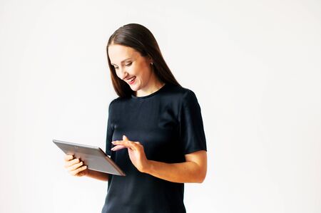 Beautiful girl in black t-shirt with a tablet in hands, her fingers on touchscreen isolated on a white background. Technology, gadgets conceptの写真素材
