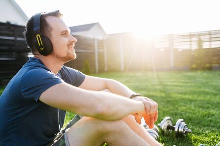 A young attractive athletic guy in headphones listens music while taking a break between workout sets. Healthy lifestyle concept. Close-up portraitの写真素材