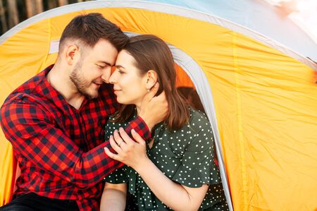 Couple in love spend time in a camp in the forest, they are sitting and hugging in an orange tent. Tourists, campersの写真素材