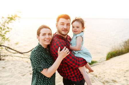 Tender shot of family outdoors. A young mother and father with their cute daughter spend time together on the lakeの写真素材